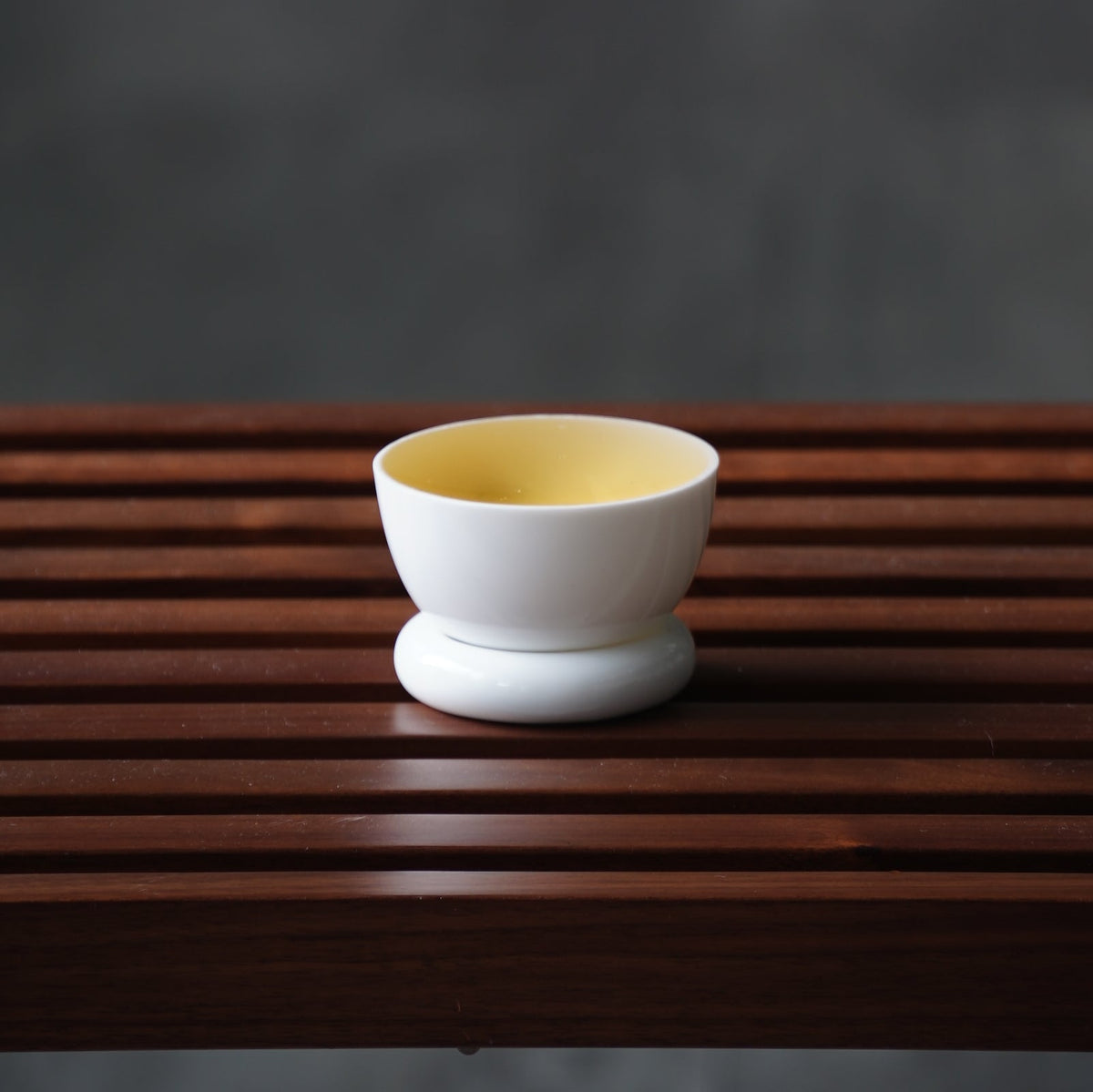 圓好夢白瓷茶杯盛裝金黃茶湯,圓形杯托置於深色木格茶盤