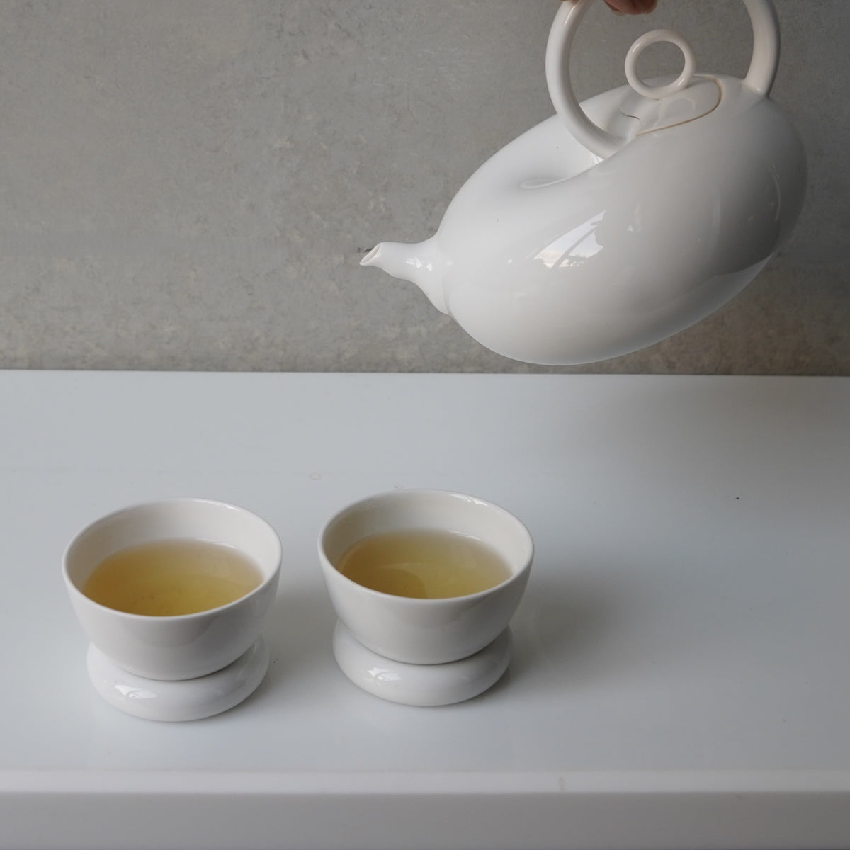 圓好夢白瓷茶壺斟茶情境,茶湯注入兩只置於圓形杯托上的茶杯