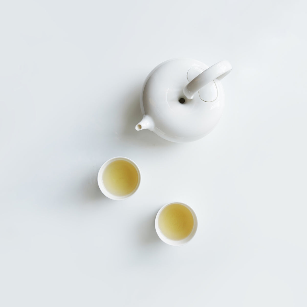 圓好夢白瓷茶壺與兩只茶杯俯視圖,純白茶器盛裝金黃色茶湯