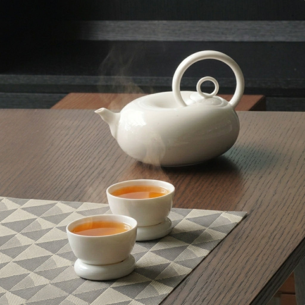 圓好夢白瓷茶具一壺兩杯組,渾圓壺身與環形把手陳列於深色木質茶桌