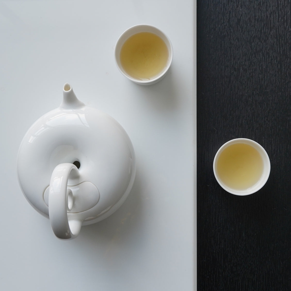 圓好夢白瓷茶具俯視構圖,圓形茶壺跨越明暗桌面並搭配兩只品茗杯