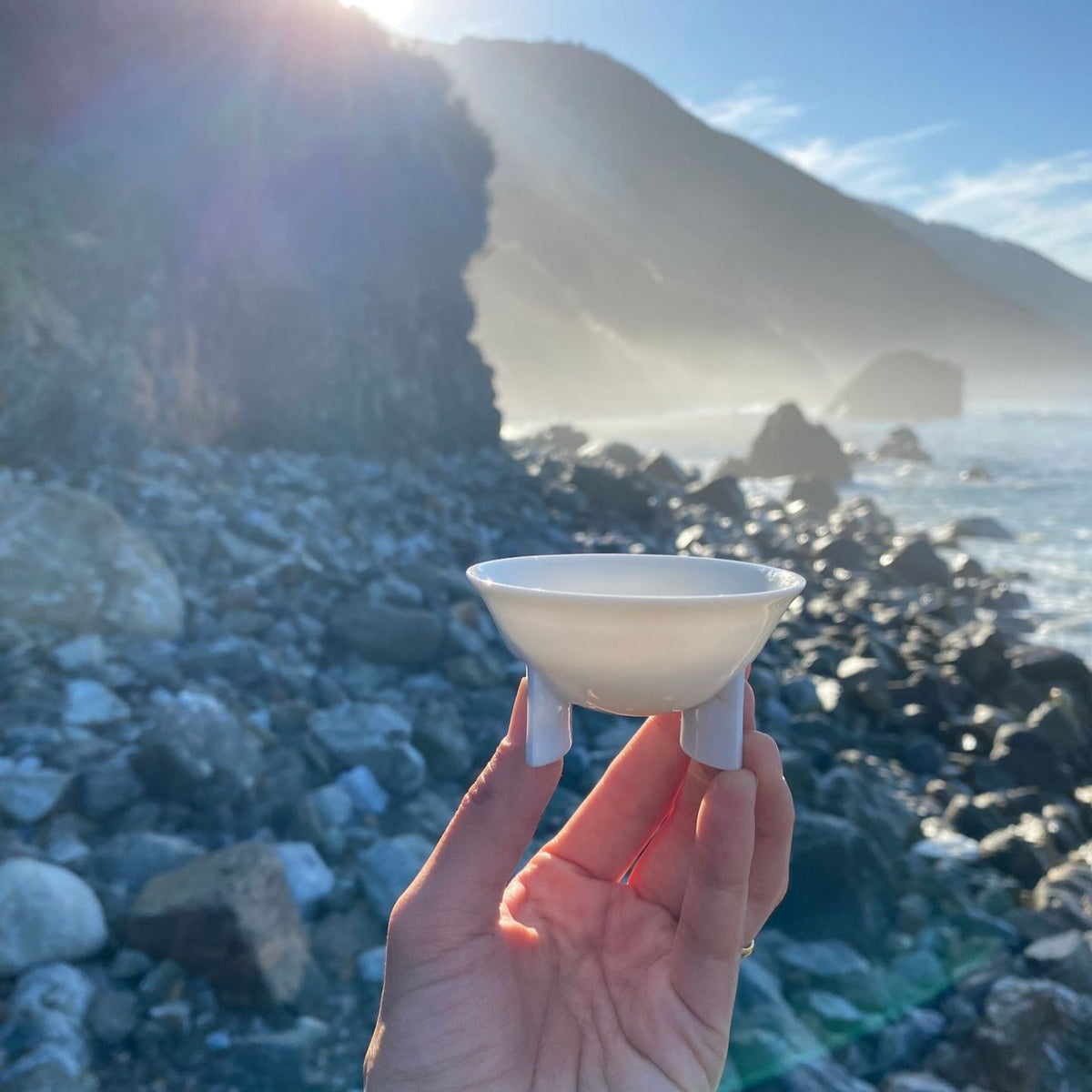 手持〈如意雲遊〉茶杯,背景是海岸