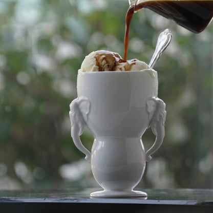 萬象一新精緻的雙象耳白瓷杯，完美盛裝上一份經典的義式甜點 Affogato（阿芙佳朵）濃郁、高溫的 Espresso 緩緩澆淋在冰涼細緻的香草冰淇淋上，沿著瓷器優雅的弧度流淌，展現出冷與熱、黑與白的極致交融。