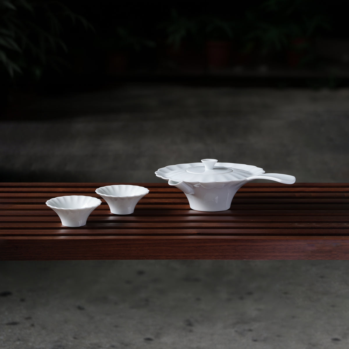 〈山水情深〉茶壺與兩只茶杯並列於木長凳，庭院夜景