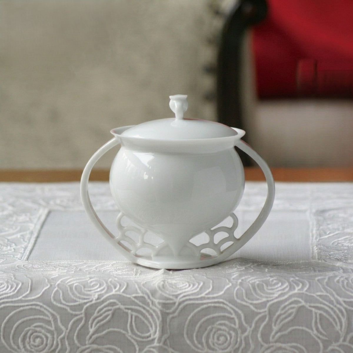 八方新氣〈滿庭芳〉白瓷蓋杯，雙弧杯把與窗櫺鏤空底座，蕾絲桌巾上