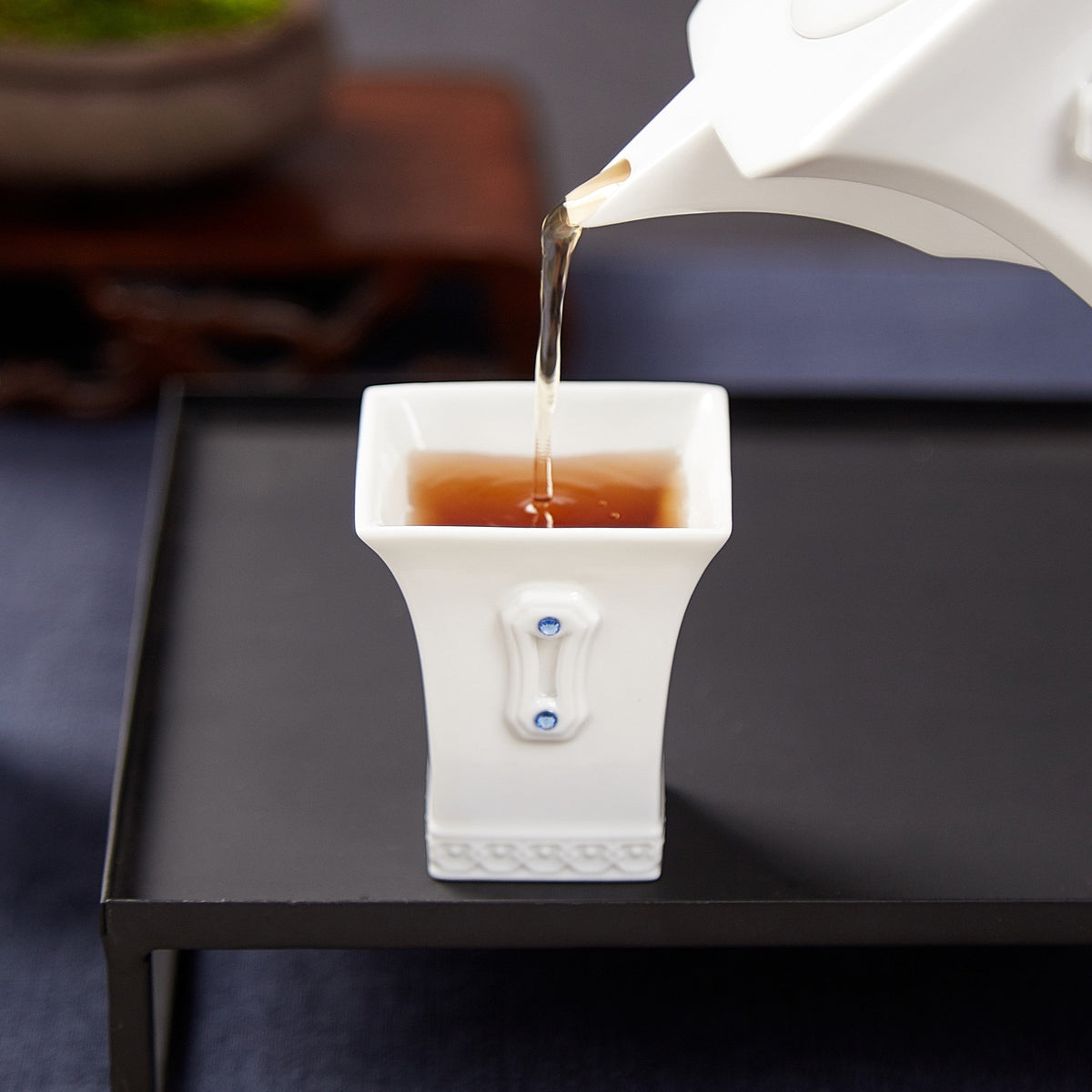 明珠在握白瓷茶壺斟入方口茶杯，展示茶具出水表現與杯身水鑽細節
